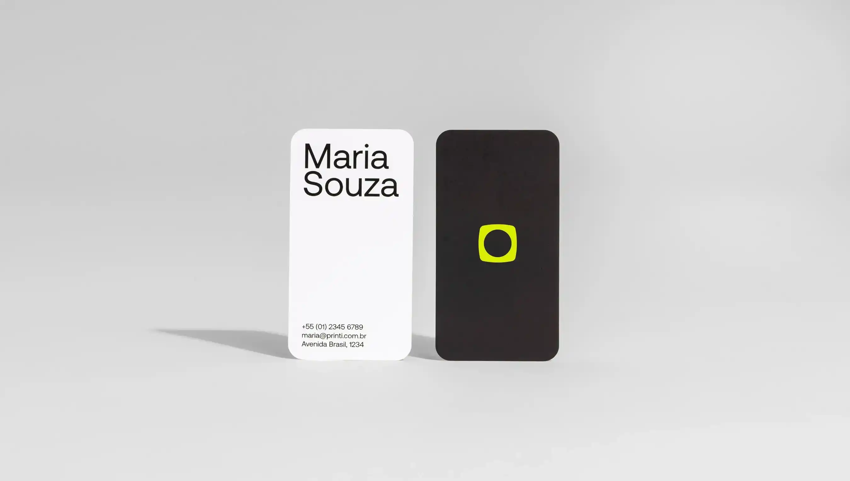 um cartao de visita branco com o nome de maria souza em pé ao lado de outro cartão de visita preto com o logo da printi na cor verde
